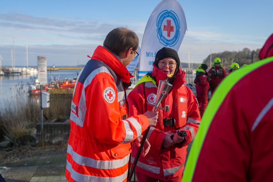 Mehrere Menschen in DRK-Einsatzkleidung stehen an einem Hafen. Im Hintergrund weht eine DRK-Wasserwacht-Fahne.