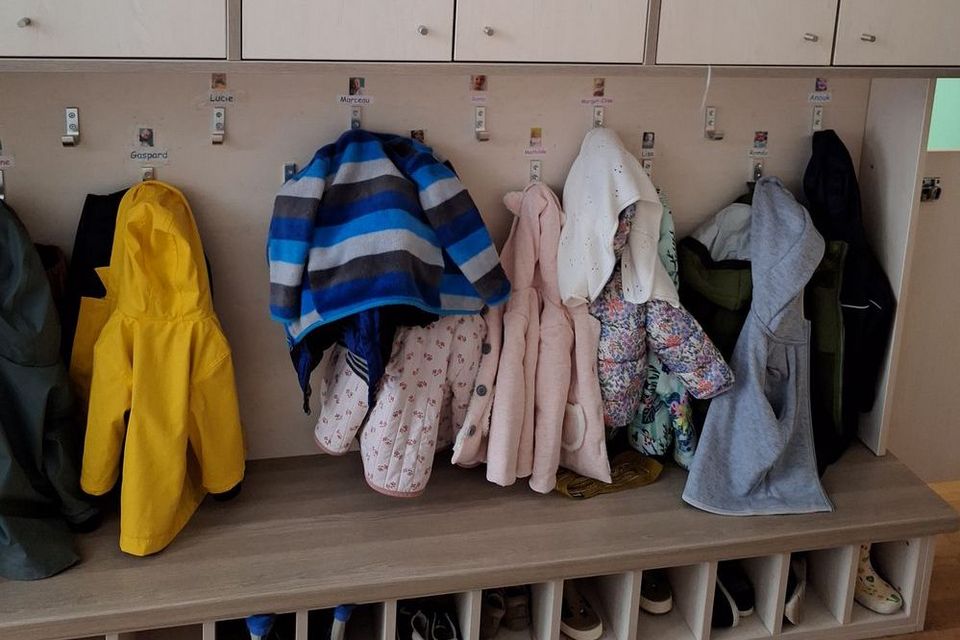 Blick in eine Krippe: An einer Garderobe hängen zahlreiche Kinderjacken. Darunter stehen Schuhe in einzelnen Fächern.