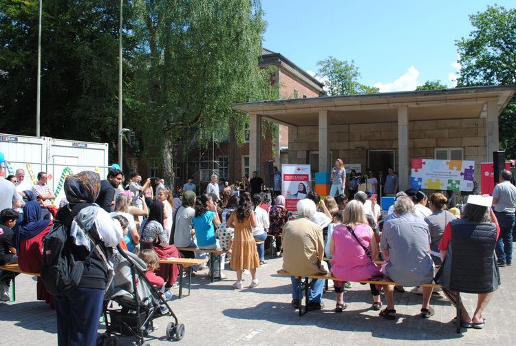 Sommerfest 2025 Eine Person steht auf einer Bühne und spricht zu rund 50 Leuten.