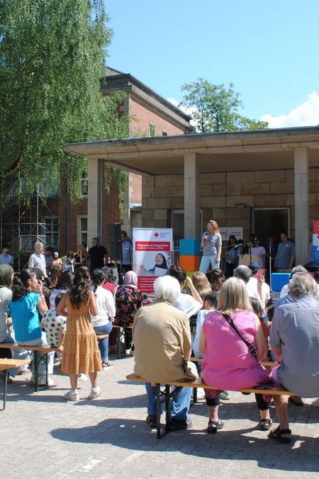 Sommerfest 2025 Eine Person steht auf einer Bühne und spricht zu rund 50 Leuten.