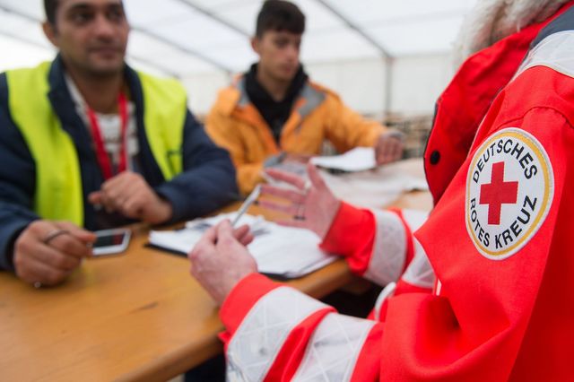 In einem großen Zelt spricht eine Person vom Deutschen Roten Kreuz mit zwei Menschen mit Migrationshintergrund.