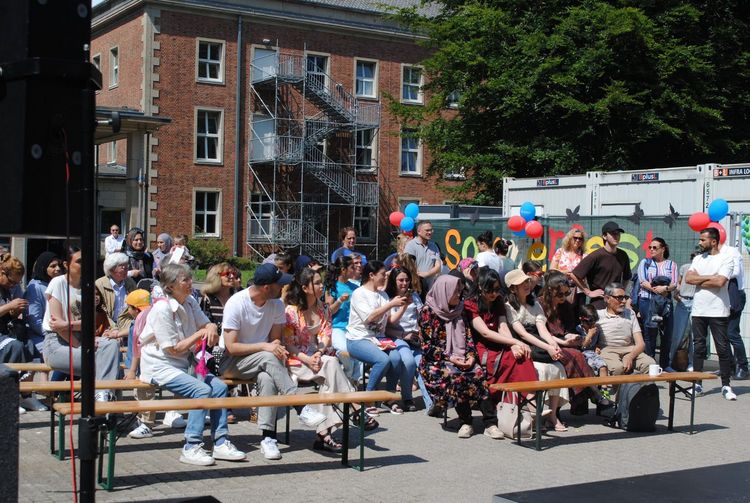 Sommerfest 2025 Rund 50 Leute sitzen auf Bänken vor einer Bühne.