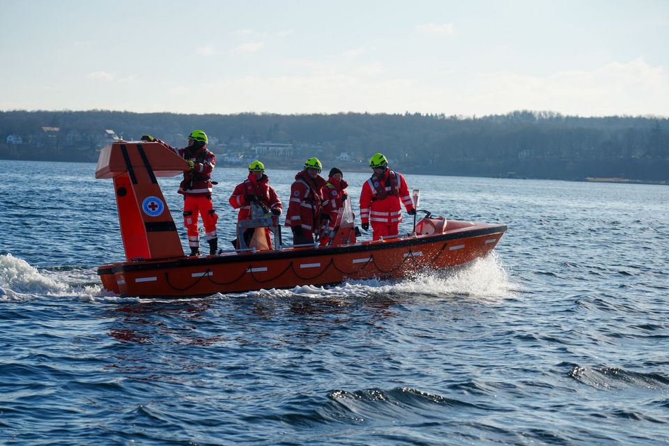 An Bord eines orangefarbenen Rettungsbootes überqueren 5 Personen in DRK-Einsatzkleidung die Flensburger Förde.