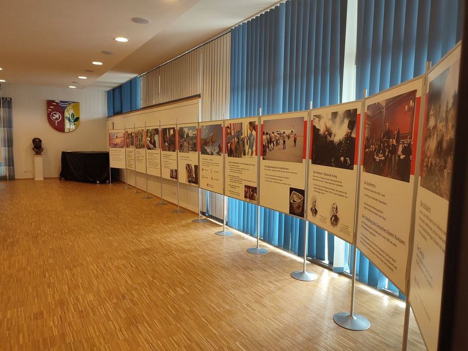 DRK-Wanderausstellung In einem großen Saal steht eine lange Reihe von großen Stellwänden. Sie zeigen die Geschichte des humanitären Völkerrechts.